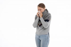 A woman with a cold blowing her nose and wearing heavy clothes
