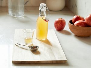 wooden board with apple cider vinegar, apples and a spoon on it